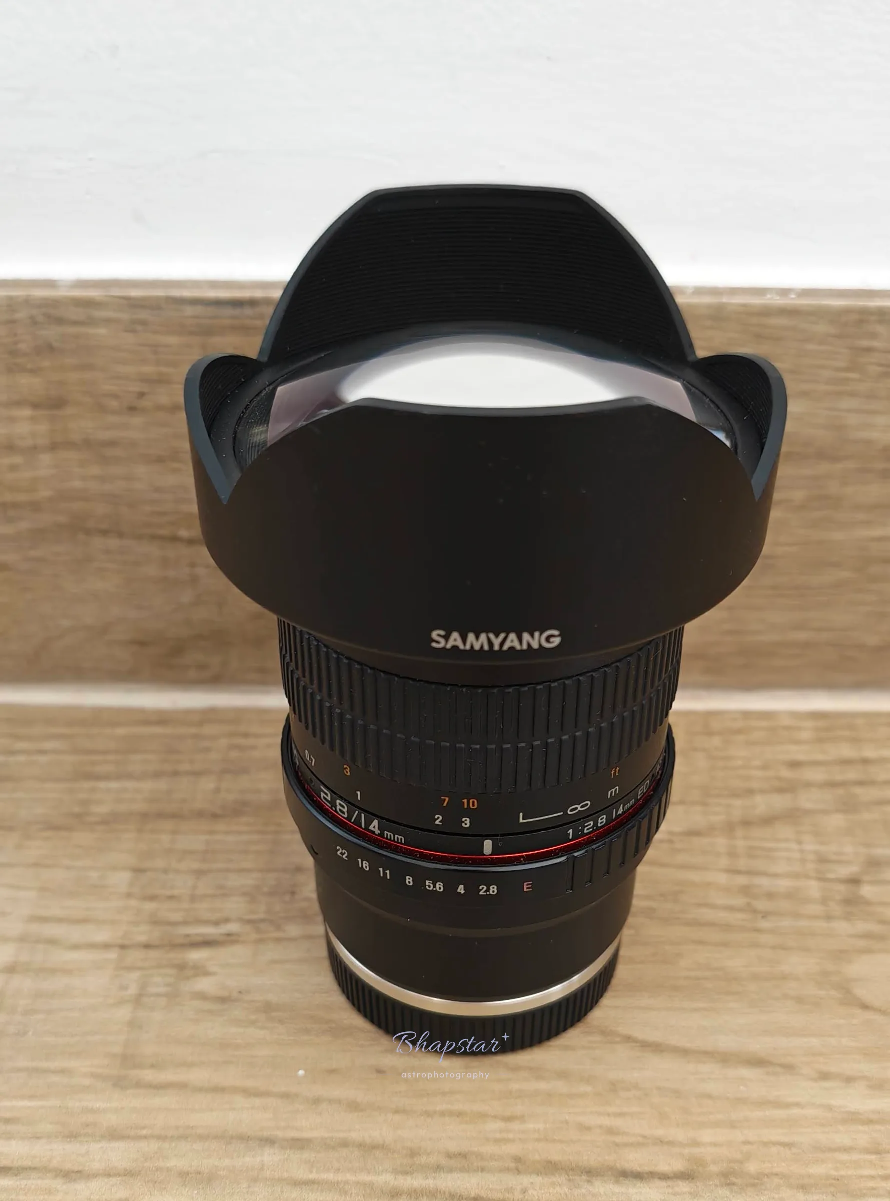 Samyang 14mm f/2.8 manual ultra-wide lens standing upright, with its fixed petal hood and the focus and aperture scales